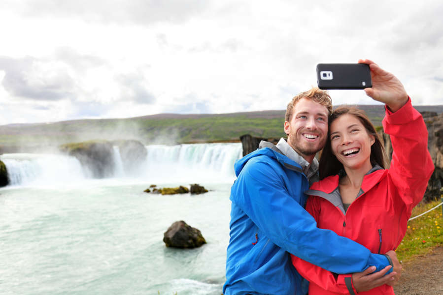 Couple using mobile networks in Iceland and taking a photo at a waterfall