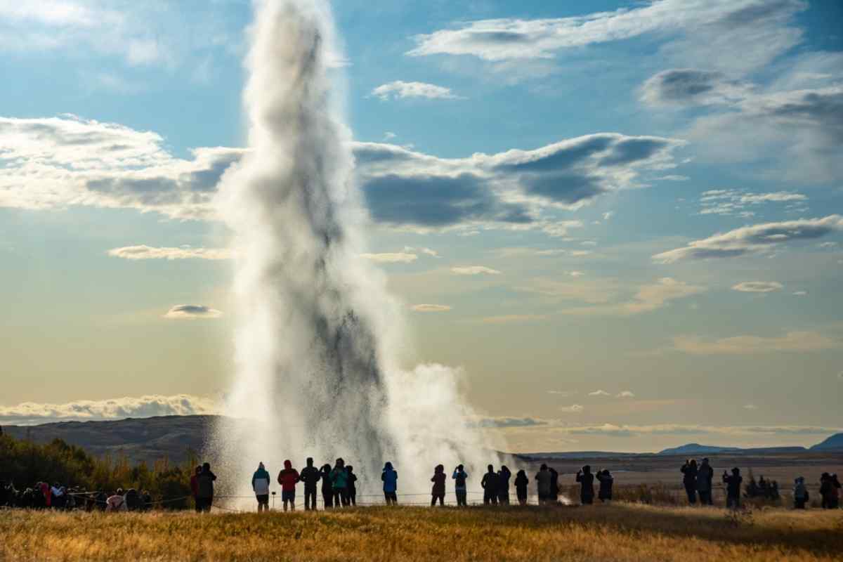 Turistas observando la erupción del géiser Strokkur en el Círculo Dorado de Islandia durante el atardecer.