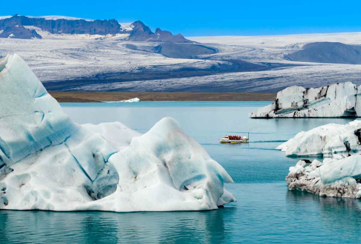 Barco entre icebergs en la laguna glaciar de Jökulsárlón, Islandia, con montañas nevadas al fondo.