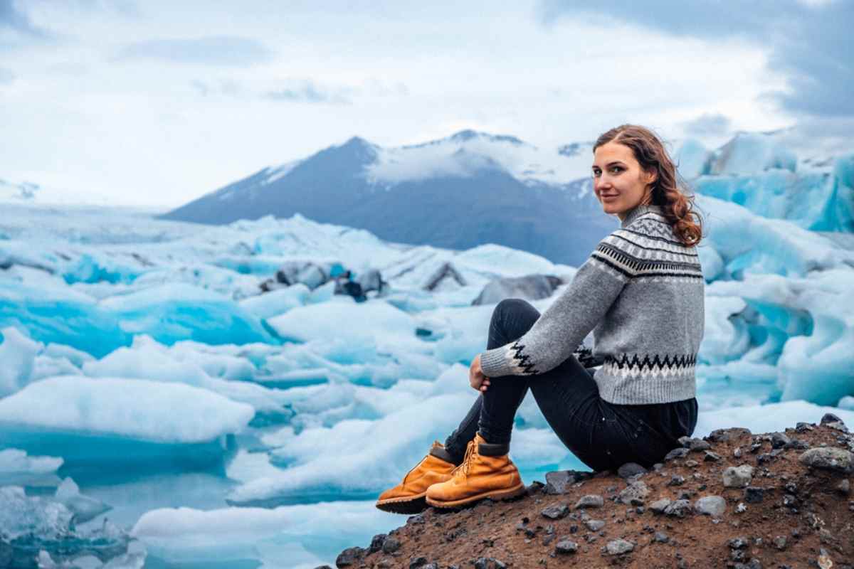 Mujer con suéter islandés sentada frente a los icebergs de la laguna glaciar Jökulsárlón.