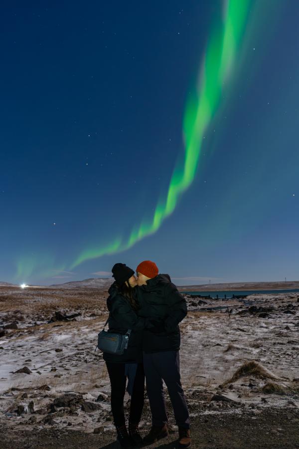 Pareja besándose bajo las auroras boreales en un paisaje nevado islandés de noche