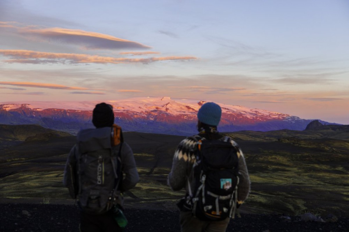 Dos senderistas con mochilas contemplando las Highlands de Islandia al atardecer